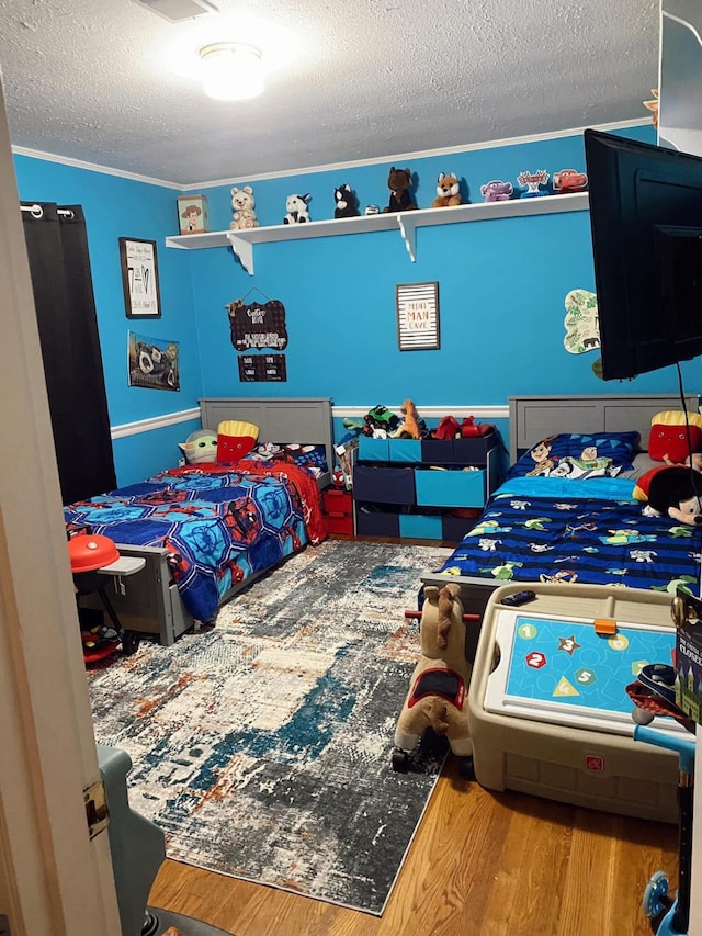 bedroom featuring crown molding, wood finished floors, visible vents, and a textured ceiling