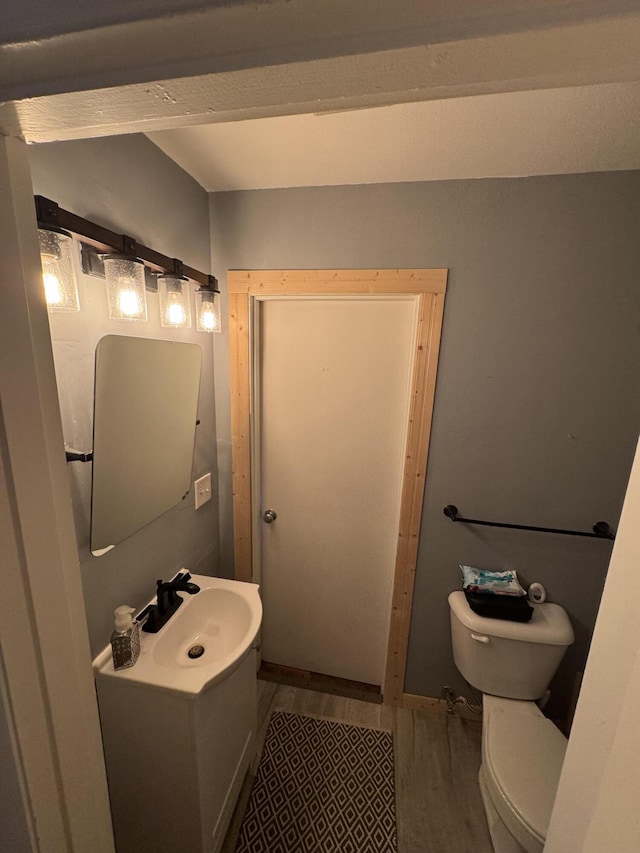 half bathroom with vanity, toilet, and wood finished floors