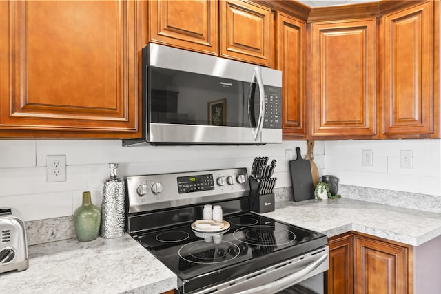 kitchen featuring brown cabinets, backsplash, appliances with stainless steel finishes, and light countertops