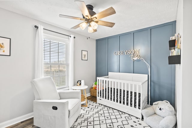 bedroom with baseboards, wood finished floors, a decorative wall, a textured ceiling, and a nursery area