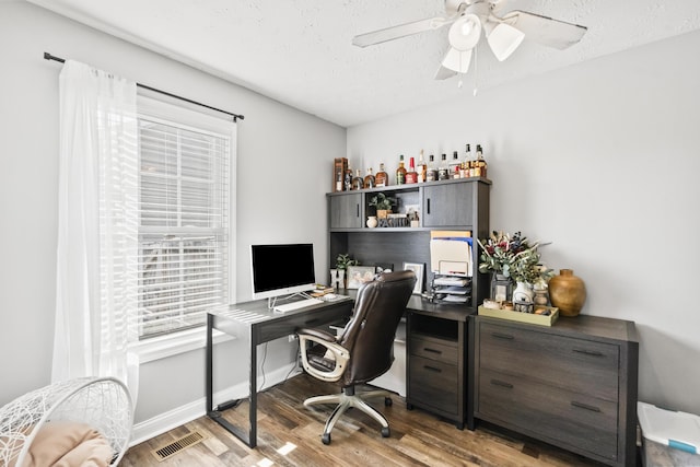 office space with visible vents, a textured ceiling, light wood-style floors, baseboards, and ceiling fan