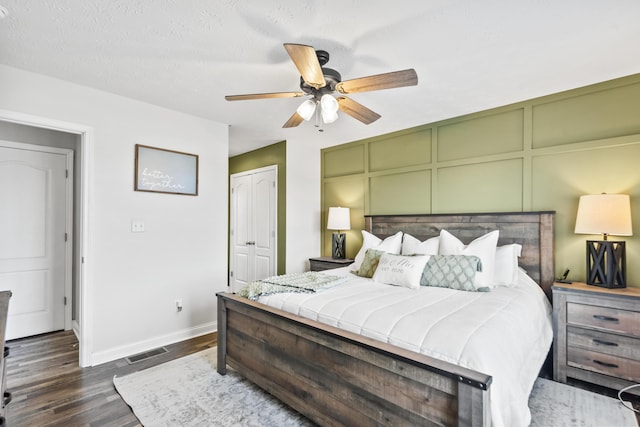 bedroom with visible vents, baseboards, ceiling fan, dark wood-style floors, and a decorative wall