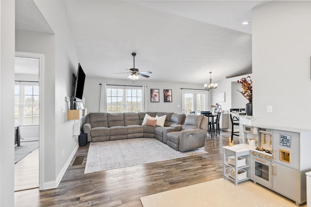 living room featuring visible vents, ceiling fan with notable chandelier, wood finished floors, baseboards, and vaulted ceiling