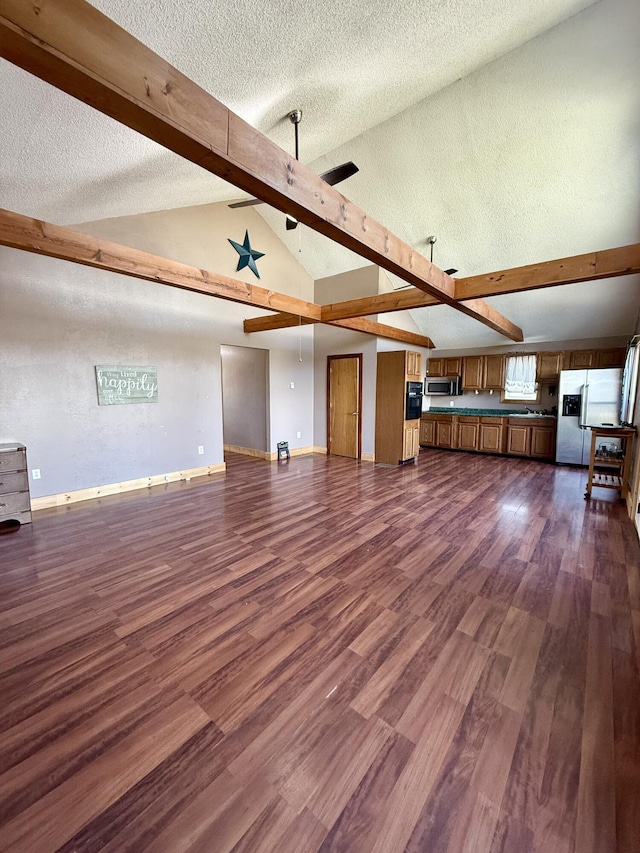 unfurnished living room featuring beam ceiling, dark wood-type flooring, a ceiling fan, and a textured ceiling