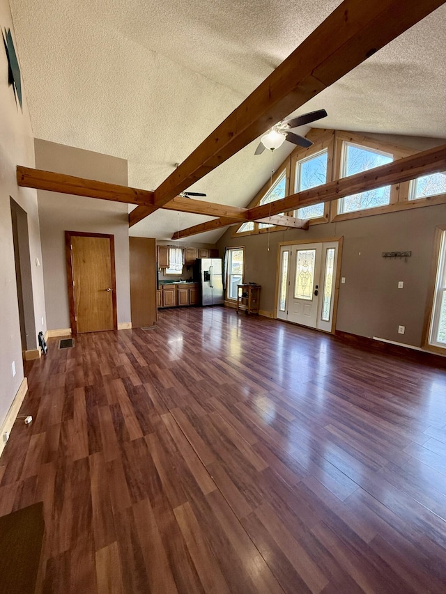 unfurnished living room with beamed ceiling, wood finished floors, baseboards, and a textured ceiling