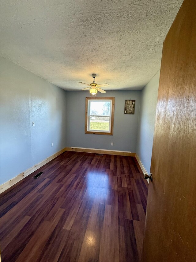 spare room featuring visible vents, dark wood-type flooring, baseboards, a textured ceiling, and a ceiling fan