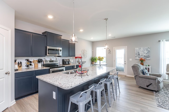 kitchen featuring a breakfast bar area, light stone counters, a sink, stainless steel appliances, and backsplash