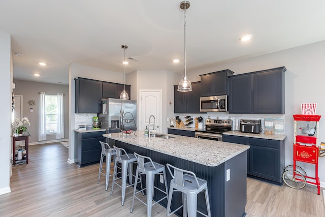 kitchen with a center island with sink, a breakfast bar, light wood-style floors, stainless steel appliances, and a sink