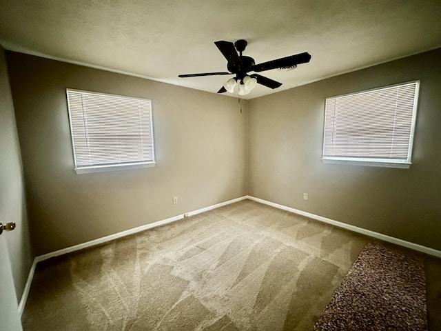 carpeted empty room featuring a ceiling fan, baseboards, and a wealth of natural light