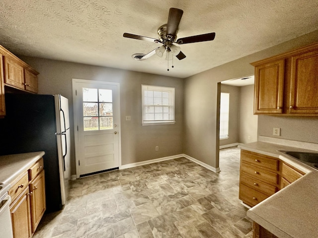 kitchen with brown cabinets, a ceiling fan, a sink, freestanding refrigerator, and baseboards