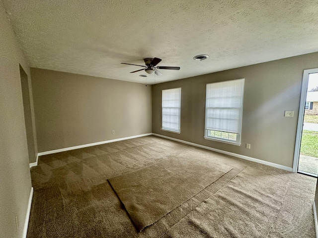 carpeted spare room with a ceiling fan, visible vents, baseboards, and a textured ceiling