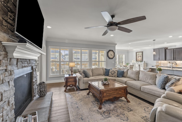 living room featuring recessed lighting, a stone fireplace, wood finished floors, and crown molding