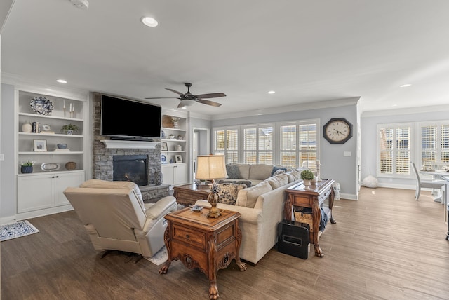 living area featuring a stone fireplace, crown molding, wood finished floors, and baseboards