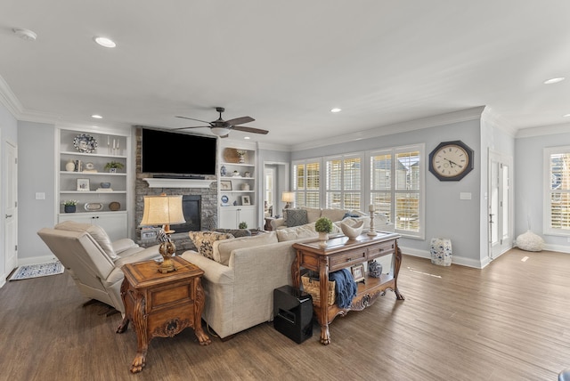 living area with a stone fireplace, a healthy amount of sunlight, crown molding, and wood finished floors