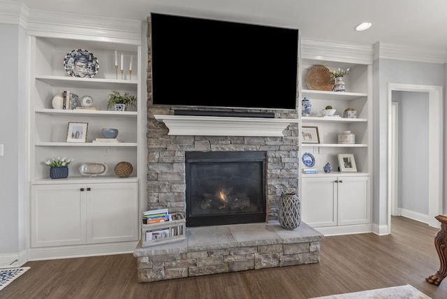 living room with built in shelves, wood finished floors, baseboards, ornamental molding, and a stone fireplace