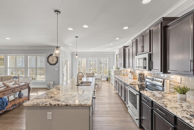 kitchen with ornamental molding, a sink, open floor plan, appliances with stainless steel finishes, and decorative backsplash