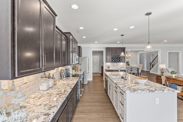 kitchen with ornamental molding, a sink, light stone counters, stainless steel appliances, and dark brown cabinetry