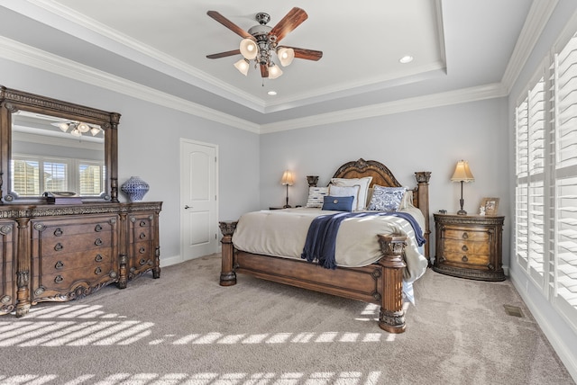 carpeted bedroom with visible vents, a tray ceiling, crown molding, baseboards, and ceiling fan