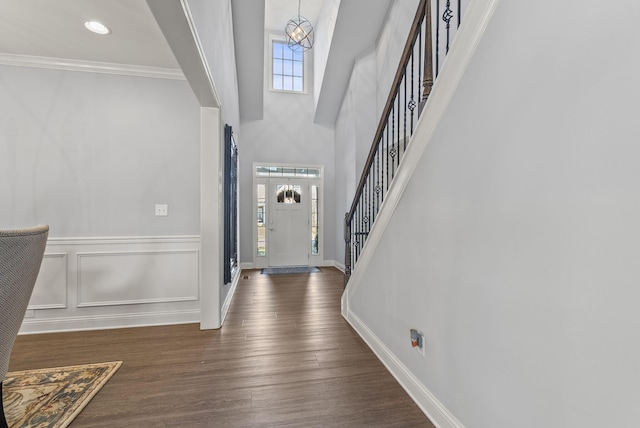 entryway with ornamental molding, dark wood-style floors, stairway, a decorative wall, and a chandelier