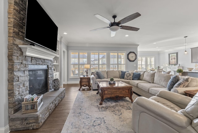 living area with wood finished floors, recessed lighting, ceiling fan, a stone fireplace, and crown molding