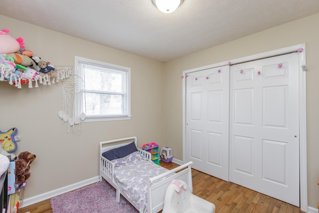 bedroom featuring light wood-style floors, baseboards, a closet, and a textured ceiling