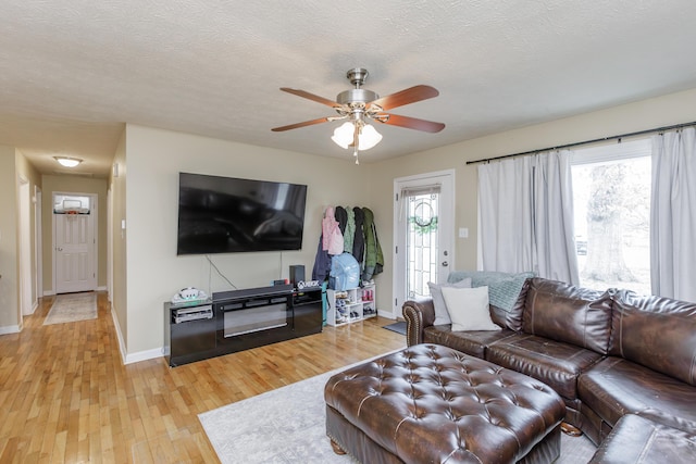 living room featuring light wood finished floors, baseboards, a textured ceiling, and ceiling fan