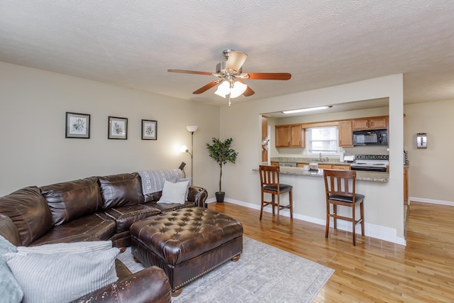 living area featuring light wood-type flooring, baseboards, a textured ceiling, and ceiling fan