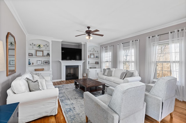 living area featuring built in features, a fireplace, crown molding, and wood finished floors