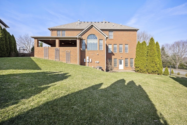 rear view of house with brick siding, a yard, and fence