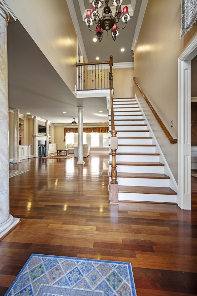 stairway featuring crown molding, a high ceiling, a fireplace, and ornate columns