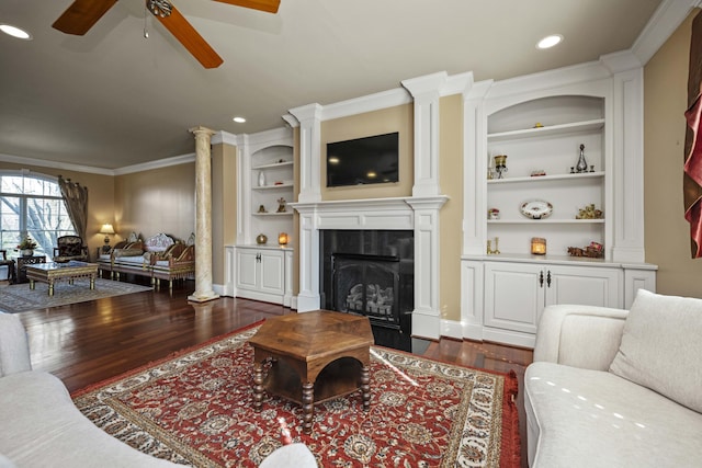 living area with built in features, dark wood-style flooring, crown molding, and ornate columns