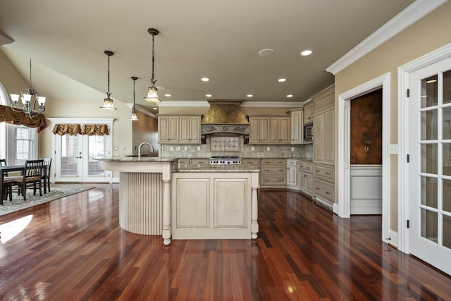 kitchen featuring custom exhaust hood, light stone counters, cream cabinetry, and a kitchen island with sink