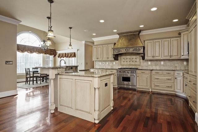 kitchen with cream cabinetry, a center island with sink, custom range hood, backsplash, and stainless steel stove