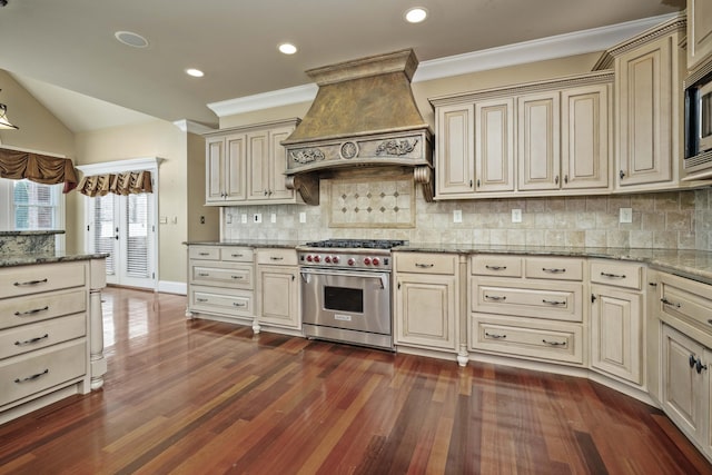 kitchen with stone counters, dark wood-style floors, cream cabinets, custom exhaust hood, and stainless steel appliances