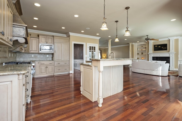 kitchen featuring a fireplace, a sink, stainless steel appliances, cream cabinetry, and open floor plan