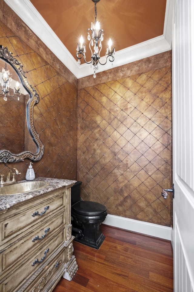 bathroom featuring a notable chandelier, wood finished floors, crown molding, baseboards, and vanity