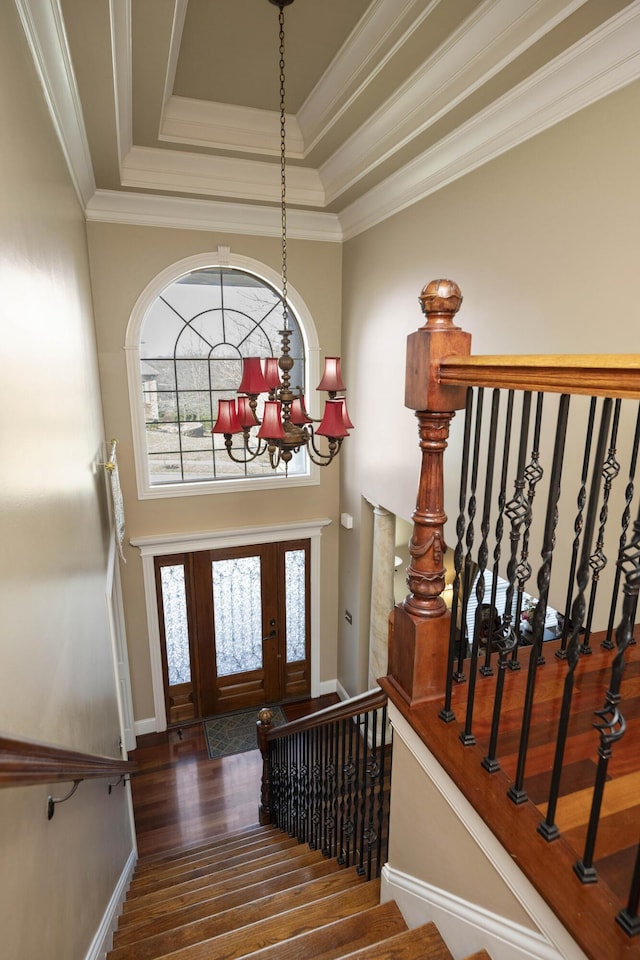 entrance foyer with wood finished floors, ornamental molding, stairs, a towering ceiling, and a chandelier