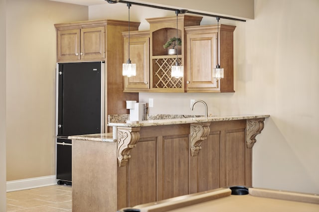 kitchen with black refrigerator, baseboards, a breakfast bar area, light stone counters, and a peninsula