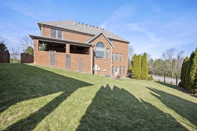 back of house with brick siding, a lawn, and fence