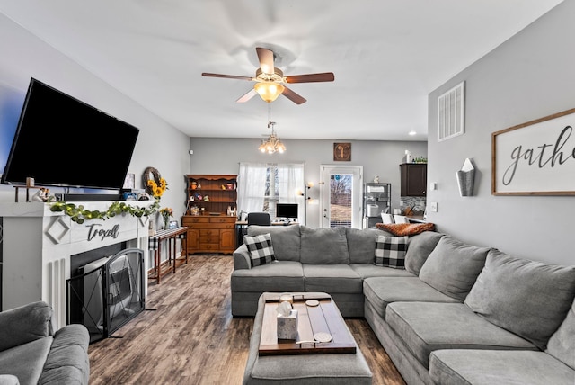 living area with visible vents, ceiling fan with notable chandelier, a fireplace, and wood finished floors