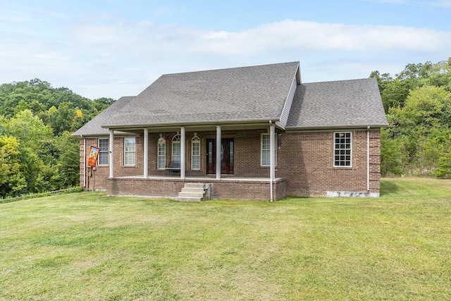 view of front of house featuring a shingled roof, covered porch, a front yard, and brick siding