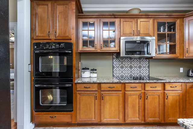 kitchen featuring light stone counters, brown cabinetry, black appliances, glass insert cabinets, and ornamental molding