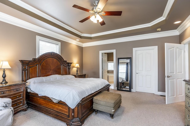 bedroom with a tray ceiling, a ceiling fan, ornamental molding, light carpet, and ensuite bath
