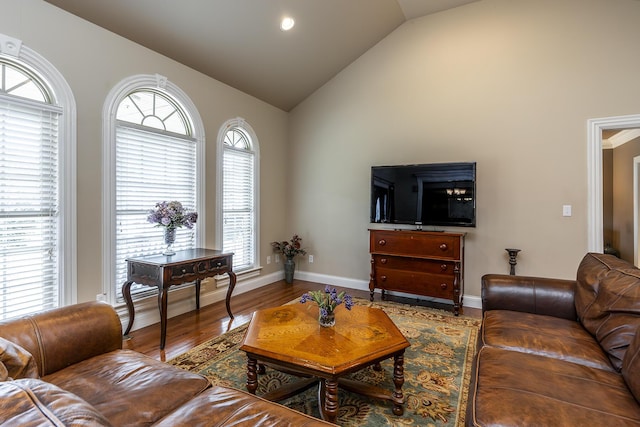living room featuring high vaulted ceiling, baseboards, and wood finished floors