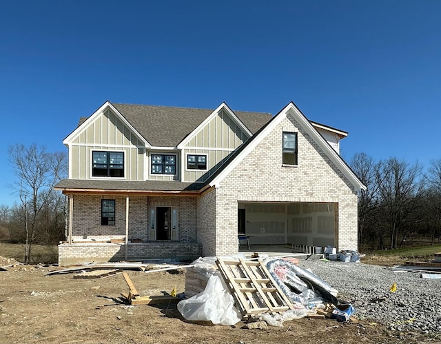 view of front of house with board and batten siding, a garage, brick siding, and a shingled roof