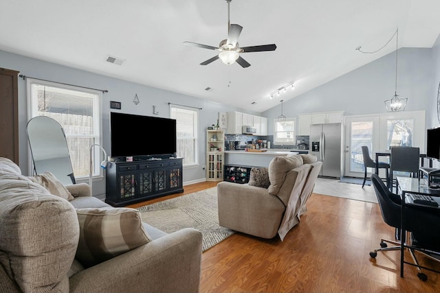 living area with visible vents, light wood-style flooring, ceiling fan with notable chandelier, and high vaulted ceiling