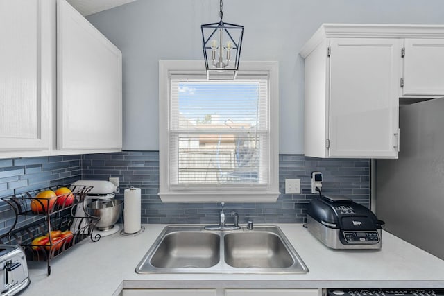 kitchen with a sink, hanging light fixtures, light countertops, white cabinets, and tasteful backsplash