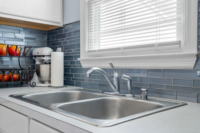 details featuring decorative backsplash, white cabinets, light countertops, and a sink