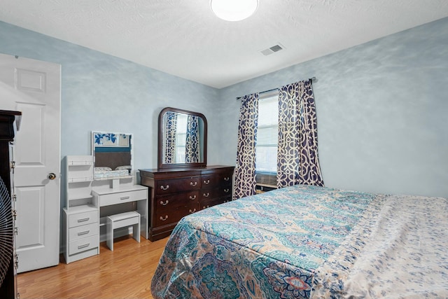 bedroom featuring light wood finished floors, visible vents, and a textured ceiling