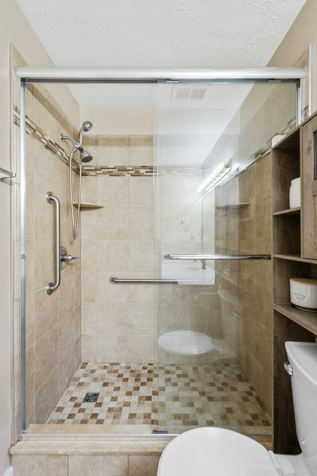 bathroom with toilet, a shower stall, and a textured ceiling